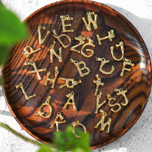 Assorted A-Z gold-tone letter pendants displayed on a wooden tray for personalized initial necklaces