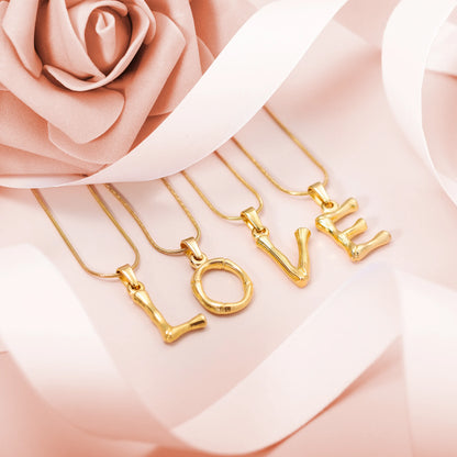 Gold-tone letter necklaces spelling LOVE with initial pendants on a soft pink floral background